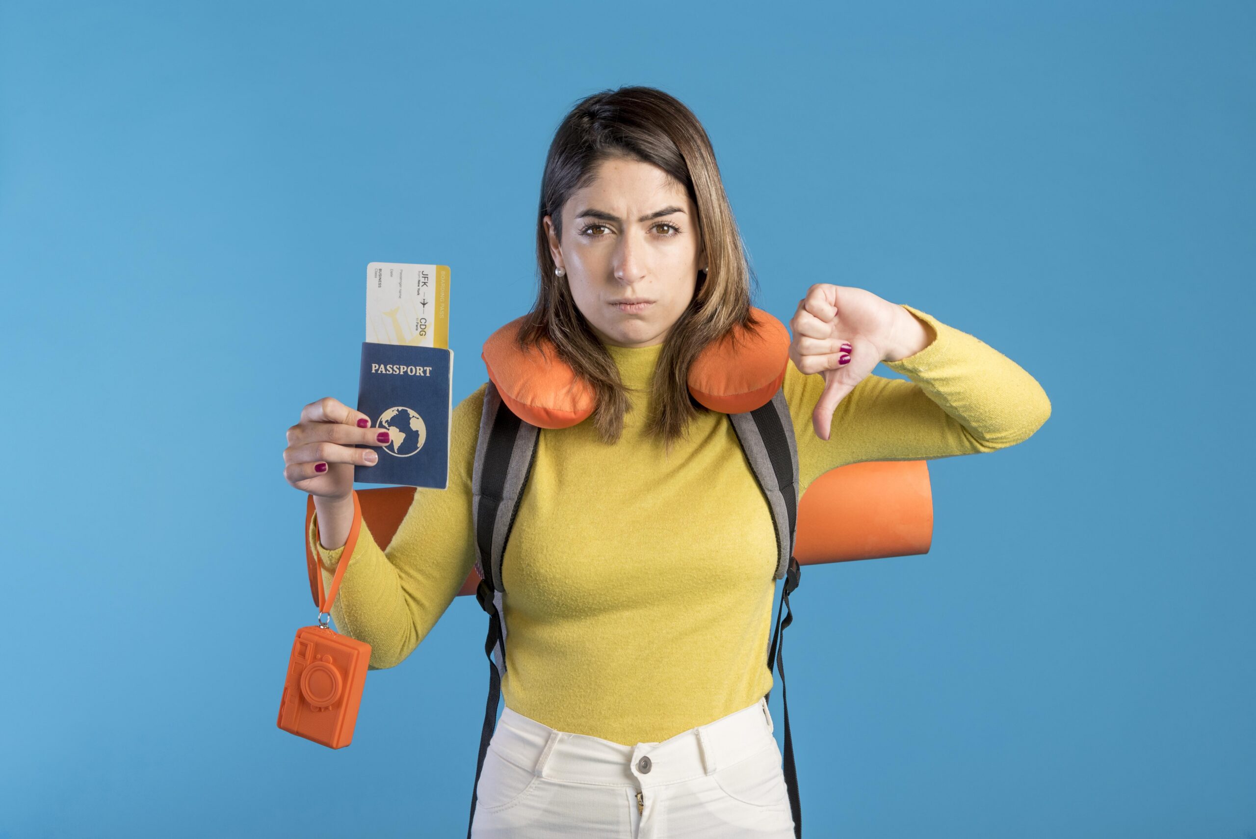 Une femme avec un coussin de voyage et un sac à dos tient un passeport et une carte d'embarquement d'une main et fait un signe du pouce vers le bas de l'autre, l'air mécontent, sur un fond bleu.